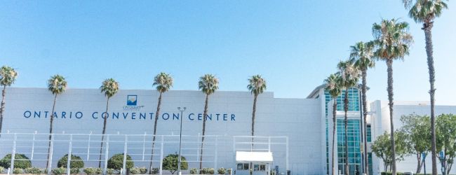 A large white convention center with &ldquo;Ontario Convention Center&rdquo; on the fa&ccedil;ade, palm trees lining the front, and a clear blue sky.